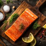 A beautifully smoked salmon fillet on a wooden cutting board, surrounded by brining ingredients like salt, sugar, and dill.