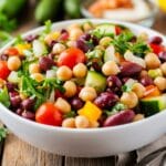 Salade de haricots dense avec pois chiches, haricots rouges, légumes frais et persil dans un bol blanc.