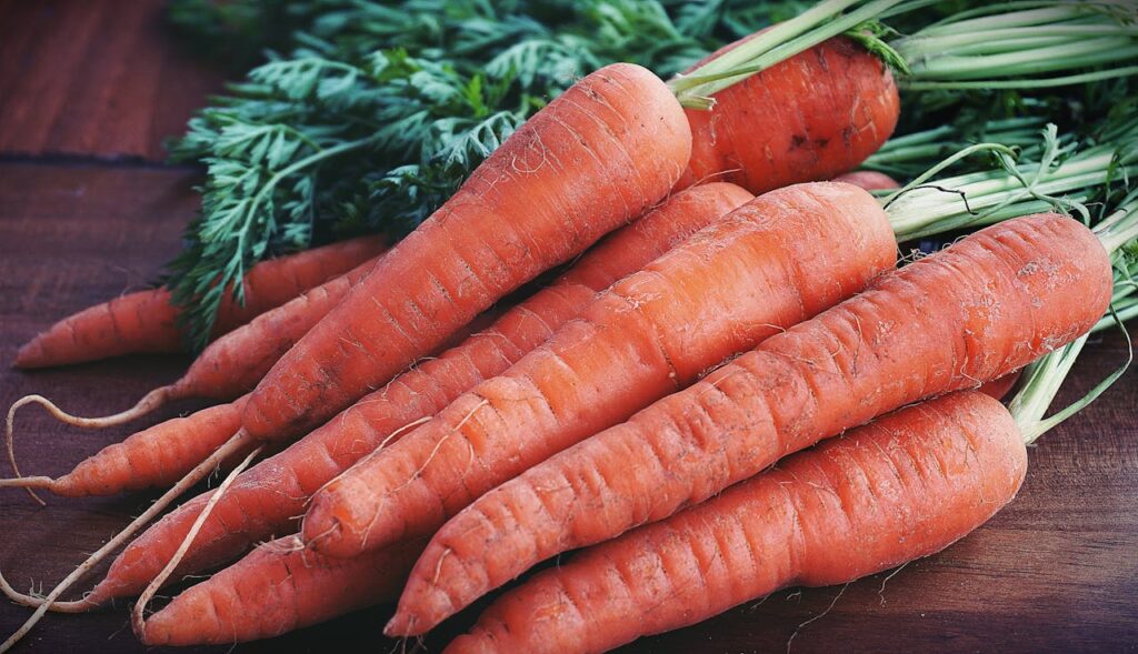 A close-up of fresh, vibrant carrots with green tops placed on a wooden surface, showcasing their natural freshness and quality