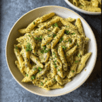 How to Make Creamy Pesto Sauce (3 Easy Variations) 5 Overhead view of penne pasta coated in creamy pesto sauce, topped with fresh parsley and cracked black pepper in a white ceramic bowl.