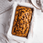 Pumpkin Bread with Chocolate Chips – Easy & Delicious 7 Golden brown chocolate chip pumpkin bread fresh out of the oven in a ceramic loaf pan, topped with melty chocolate chips.