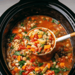 Crockpot Minestrone Soup: The Ultimate Hearty Slow Cooker Classic 5 A close-up of colorful Crockpot minestrone soup filled with vegetables, beans, and pasta, being served with a ladle from a black slow cooker.