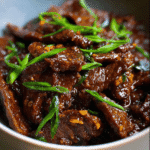 Tender slices of slow cooker Mongolian beef coated in garlic soy sauce and garnished with green onions