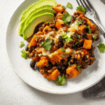 Close-up of a Southwestern Ground Beef Sweet Potato Skillet served on a white plate with melted cheese, avocado slices, and fresh cilantro.