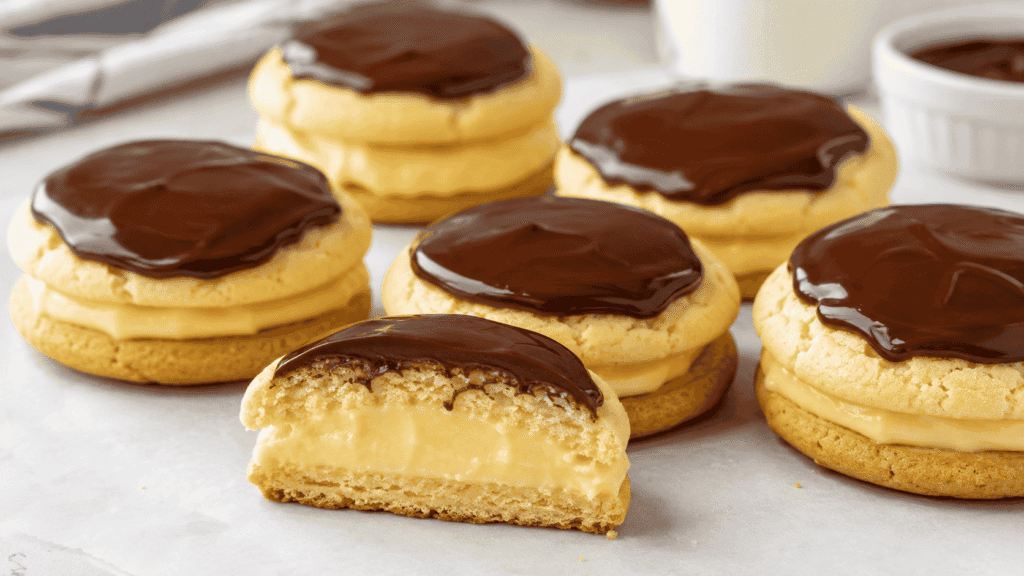 Boston Cream Pie Cookies filled with creamy vanilla pastry cream and topped with glossy chocolate ganache, with one cookie cut open. Image 2 – Ingredients and Cookie Dough