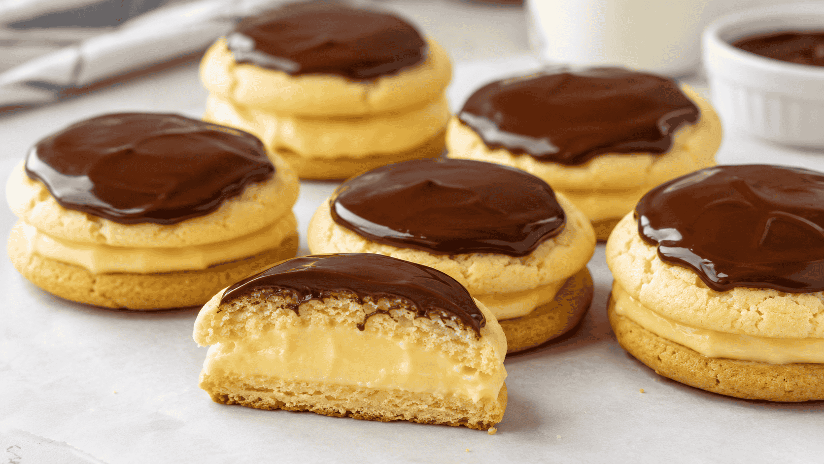 Boston Cream Pie Cookies filled with creamy vanilla pastry cream and topped with glossy chocolate ganache, with one cookie cut open. Image 2 – Ingredients and Cookie Dough