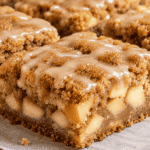Close-up of a brown butter apple blondie with tender apple chunks, cinnamon topping, and creamy cinnamon glaze.