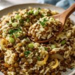 Mediterranean lentils and rice with caramelized onions, fresh parsley, and green onions served on a plate with a wooden spoon.
