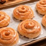 Freshly baked homemade honey buns with golden brown cinnamon swirls and a shiny sweet glaze, arranged on a parchment-lined baking sheet.