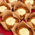 Freshly baked pumpkin cream cheese muffins with golden-brown pumpkin spice tops and rich, creamy cheesecake centers, nestled in brown parchment muffin liners.