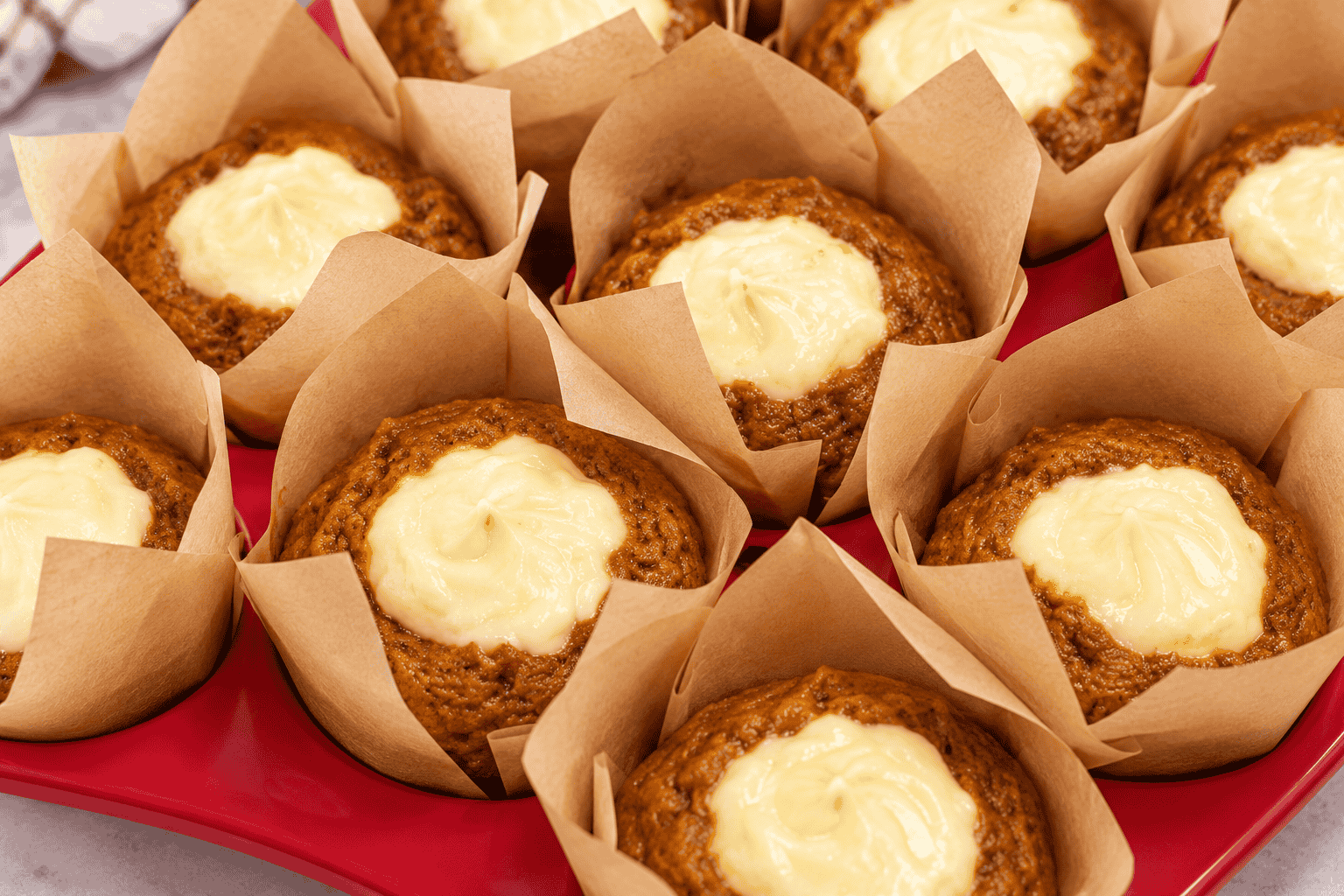 Freshly baked pumpkin cream cheese muffins with golden-brown pumpkin spice tops and rich, creamy cheesecake centers, nestled in brown parchment muffin liners.