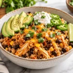 Slow cooker salsa chicken quinoa bowl with tender shredded chicken, black beans, corn, melted cheddar cheese, avocado slices, jalapeños, sour cream, fresh cilantro, and lime.