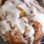 Close-up of a golden pumpkin streusel muffin with pecan topping, covered in thick vanilla glaze and resting on a cooling rack.
