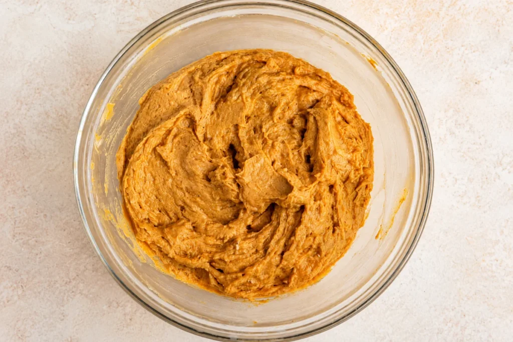 Pumpkin Streusel Muffins with Pecan Topping (Moist, Fluffy & Easy Recipe) 6 Thick orange pumpkin muffin batter mixed with warm fall spices in a clear glass mixing bowl, ready for pecan streusel topping.
